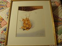 Framed watercolor painting of cluster of autumn leaves on snow, sitting on a patterned quilt.
