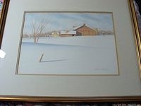 Framed watercolor painting showing a serene winter rural scene with snow and buildings.