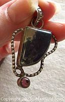 Close-up of the front side of the sterling silver pendant showing the irregular moss agate gemstone, detailed silver frame, and the tiny purple stone cabochon at the bottom.