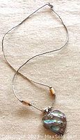 Full view of the necklace laid flat showing the liquid silver chain and abalone heart pendant with beads.