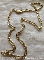 Full view of the 14K yellow gold Figaro chain laid on fabric background