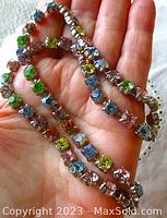 Close-up hand holding silver-tone necklace with pastel rhinestones in pink, blue, purple, orange, yellow, and green