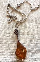 Sterling silver chain with amber pendant shown against fabric background.