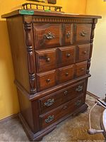 Full view of the wooden chest of drawers showing its five drawers, carved details on drawer fronts and sides, with a warm brown wood finish