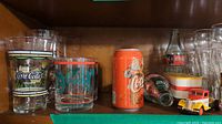Photo showing various Coca Cola drinking glasses, a vintage Santa Claus Coca Cola can, an empty glass Coca Cola bottle, and a red/yellow Coca Cola toy truck.