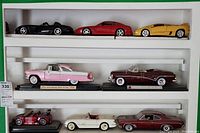 Overview of 8 die cast model cars on a white shelf, arranged in rows showing varied colors and styles.