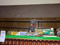 Photo showing multiple die cast vehicles including green vintage truck, yellow school bus, blue truck with trailer, and garbage trucks on shelf