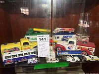 Photo showing front view of soda themed collectible trucks and glass bottles grouped together inside a display case.