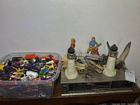 Wide view showing large bin of die cast toy cars, two lighthouse figurines, seagull figure, action figure, car model, and tape deck player