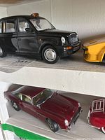 Black classic London taxi and maroon vintage coupe die cast model cars on white shelves
