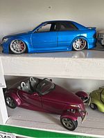 Shelf display of metallic blue lowered sedan and maroon roadster toy cars.