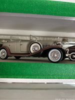 Side view of a silver and white die cast classic convertible with detailed tire spokes and chrome accents.