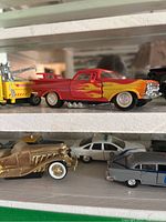 Close-up photo of a red and yellow flames pickup truck, gold vintage car, gray station wagon, and white police car on a shelf.