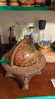 Front view showing vintage decorative globe on wooden tripod stand with longitude and latitude markings and planters decanter in background