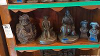 Five bronze cowboy sculptures on wooden shelf including head busts and full-figure cowboys