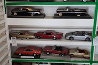 Seven miniature die cast cars arranged on shelves showing Pontiac and Chevrolet models in various colors and styles.