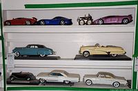 Seven miniature cars displayed on shelves showing various classic and sports car models.