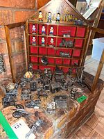 Wooden collection cabinet with red lined compartments, holding several miniature figurines and metal miniatures, some spread on the table in front.