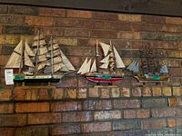 Three model ships displayed on a brick shelf: largest on left with green hull, mid-sized in center with red hull, smallest on right with blue and white striped sails.