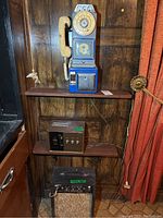 Full view of payphone mounted on wall above two amplifiers on shelves, showing overall lot contents.