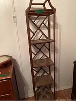 Tall rattan display shelf with four shelves and crisscross pattern on the back, brown color