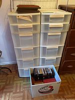 Two translucent resin drawer storage units side-by-side with a cardboard box of cassette tapes in front on floor