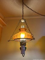 Photo of first hurricane style swag lamp lit, showing amber textured glass shade, metal frame, chain, and ceiling mount