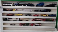 Wide shot showing multiple toy vehicles including tractor trailers, classic cars, and a city bus arranged on a white display shelf.