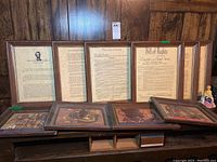 Overview photo showing six framed prints and one ceramic decorative figurine on a wooden surface against a wood-paneled wall.