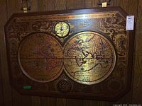 Full view of the antique-style world map printed on a circular metallic surface mounted in a carved wood frame hung on a wall.