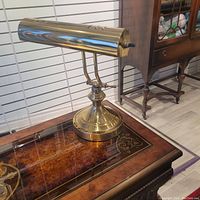 Side view of the polished brass desk lamp with cylindrical shade on a decorative wooden table.