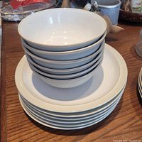 Stack of six white plates with gold rim and six matching white bowls with gold rim on top.