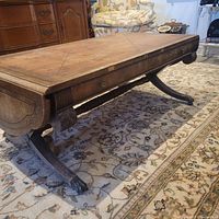 Side view of antique wooden coffee table showing carved legs, surface wear, and drawer front.