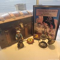 Lot of six nautical-themed items including chest, poster, figurine, barometer, tin, and lamp arranged on a white surface.