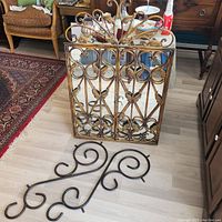 Gated rectangular mirror with ornate gold cast iron scrolling frame and opening gate with lock, placed on floor leaning on furniture.