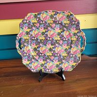 Front view of the colorful floral patterned serving tray displayed on a black stand