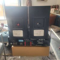 Back view of a pair of black Mission speakers showing speaker wire terminals, placed on top of the Denon receiver box.