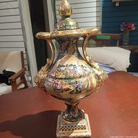 Front view of the vase showing colorful hand-painted detailed figures and gold accent handles.