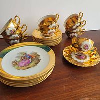 Full view of tea set showing stacked cups, saucers and plates with visible gold trim and romantic painted scenes.