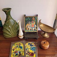 Photo of seven items: large green ceramic vase, white ceramic vase, two colorful tiles, framed elephant artwork on easel, bronze bird dish, wooden box with coasters