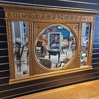 Full view of ornate gold-finished wall mirror hung on black slat wall
