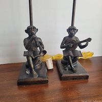 Pair of musical monkey table lamps without shades showing monkey playing clarinet and guitar figurines on bases with cords and light sockets