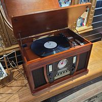 Vintage wooden stereo system with the lid open revealing a vinyl record on the turntable. Front panel includes radios, tape controls, and speakers.