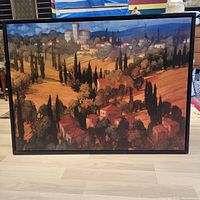 Full front view of open framed countryside landscape painting on canvas showing red roof houses, cypress trees, and hills in warm tones.