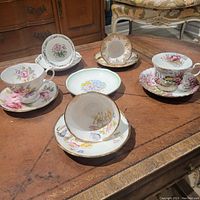View of five tea cup and saucer sets and one extra decorative plate on a wood table showing various floral patterns and gold trim.