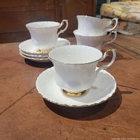 Four Royal Albert tea cup and saucer sets with matching creamers arranged on a table. White bone china with gold trim visible.