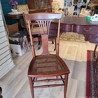 Front angle view of wooden desk chair showing cane seat and decorative backrest.