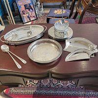Overview showing all sterling silver and crystal serving pieces arranged on a wooden desk, highlighting the variety of trays, trivets, spoons, and serving pieces.