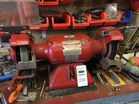Front view of the entire Baldor bench grinder-buffer showing red body, two grinding wheels with their guards, eye shields, and bench mounting base with MaxSold lot tag.