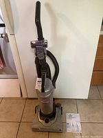 Full view of the upright vacuum cleaner with visible removable canister and hose attachment.